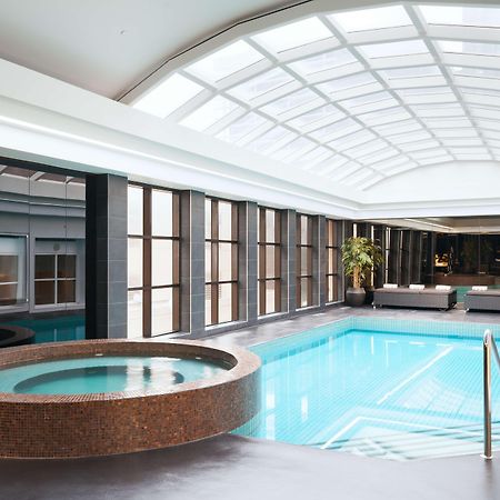 Отель Stamford Plaza Мельбурн Экстерьер фото The photo shows an indoor swimming pool area. The pool is rectangular and has clear blue water, surrounded by a sleek, modern design. On one side, there is a round hot tub made of dark stone. Large windows line the walls, allowing natural light to fi
