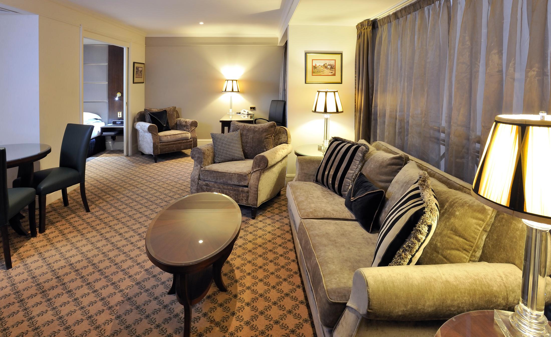 Отель Stamford Plaza Мельбурн Экстерьер фото The photo shows a stylish and comfortable living area. It features plush seating, including a sofa with decorative cushions and a couple of armchairs. There's a circular coffee table in the center of the seating arrangement. The room has soft lightin