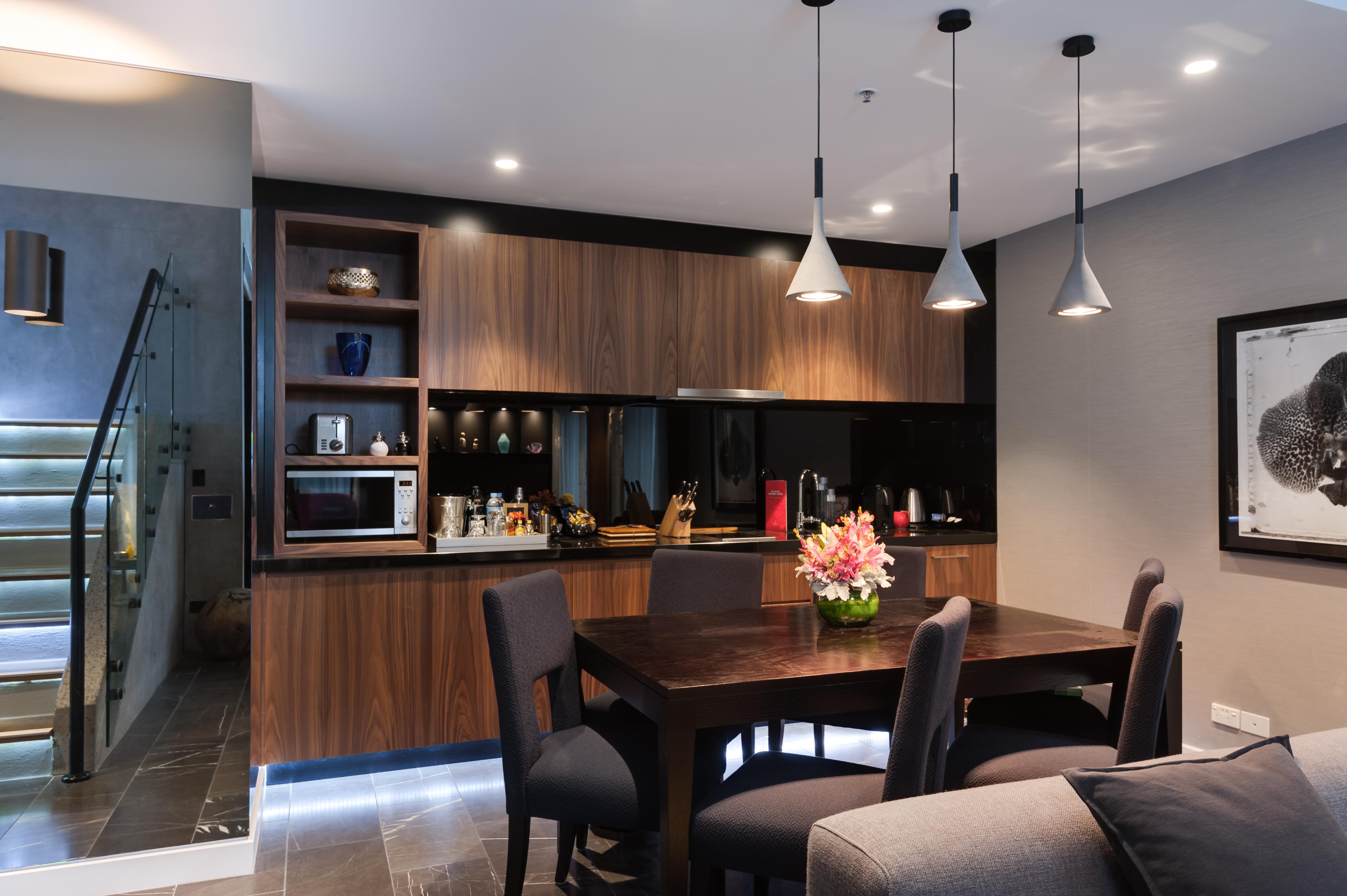 Отель Stamford Plaza Мельбурн Экстерьер фото The image shows a modern kitchen and dining area. The kitchen features dark wooden cabinetry with black accents, a microwave, and various kitchen items arranged on the shelves. There is a dining table made of dark wood, surrounded by several chairs. 