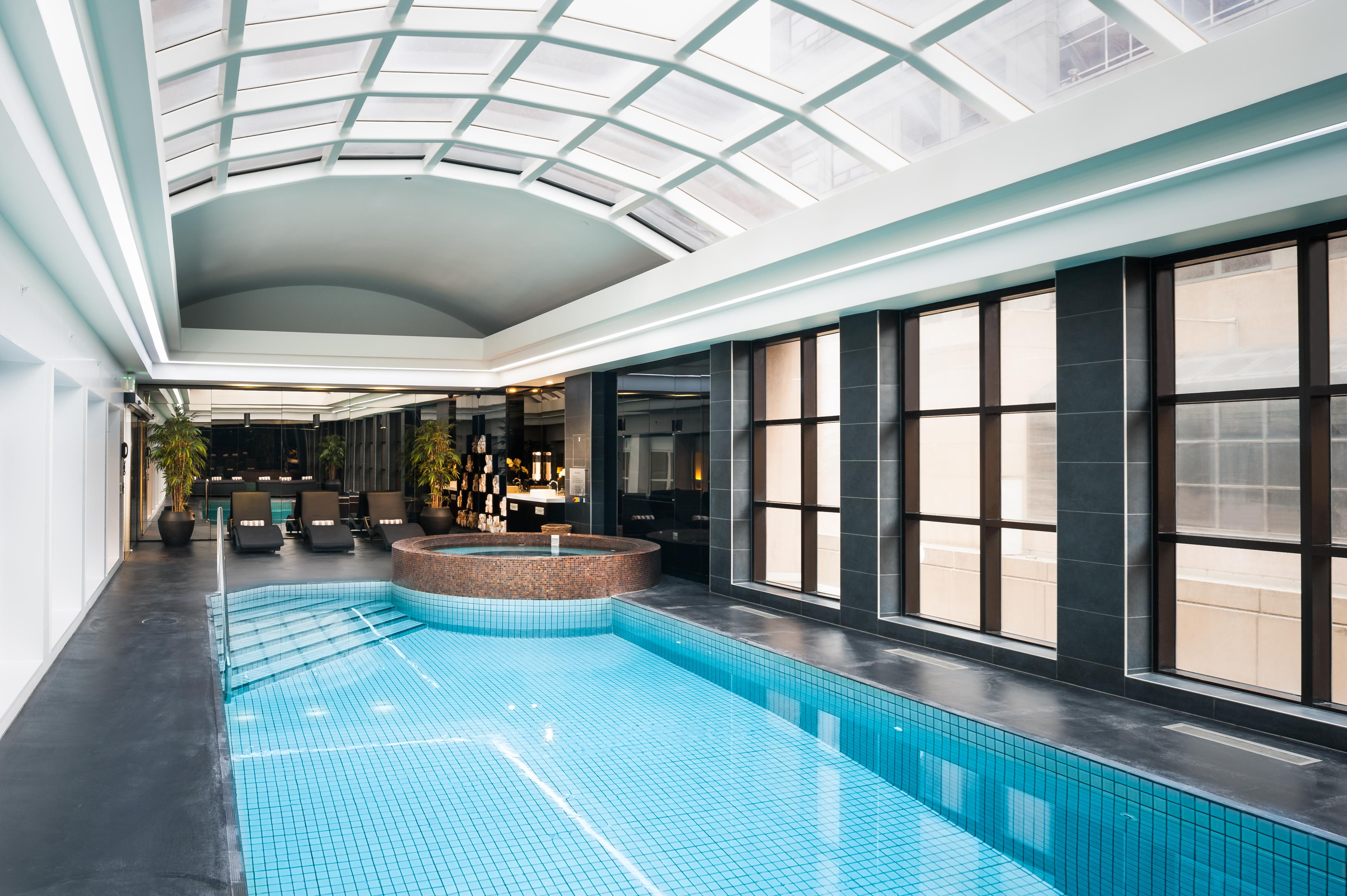 Отель Stamford Plaza Мельбурн Экстерьер фото The photo shows an indoor swimming pool area with a modern and sleek design. The pool is rectangular and features bright blue tiles. Above the pool, there's a large, transparent glass ceiling that allows natural light to flood the space. Surrounding 