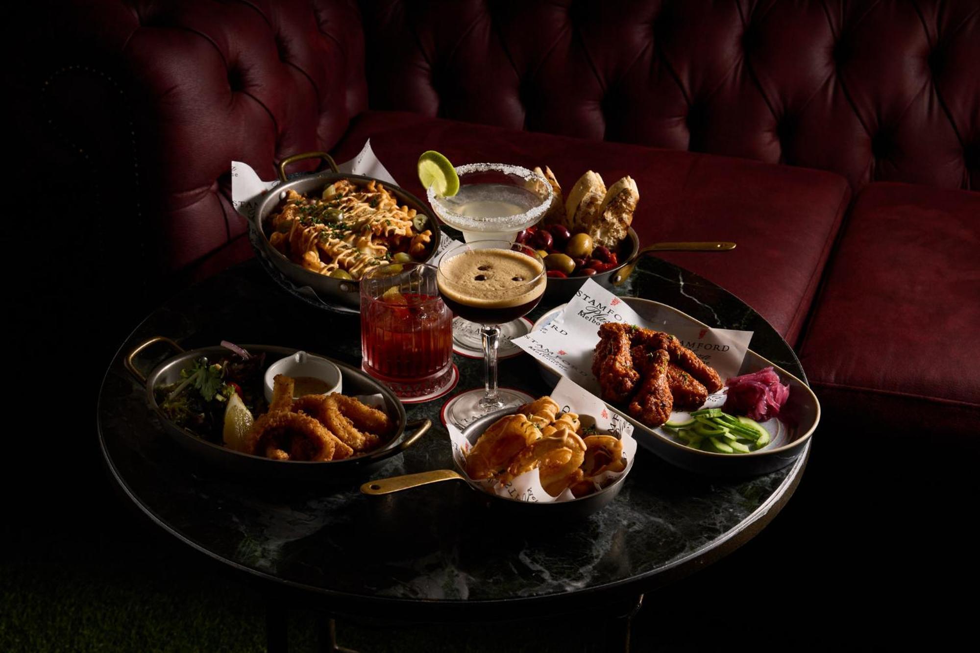 Отель Stamford Plaza Мельбурн Экстерьер фото The photo showcases a variety of delicious foods and drinks arranged on a dark marble table. There are several dishes including:

1. A large bowl of pasta with a creamy sauce.
2. A platter of chicken wings, likely spicy or barbecued.
3. A small salad