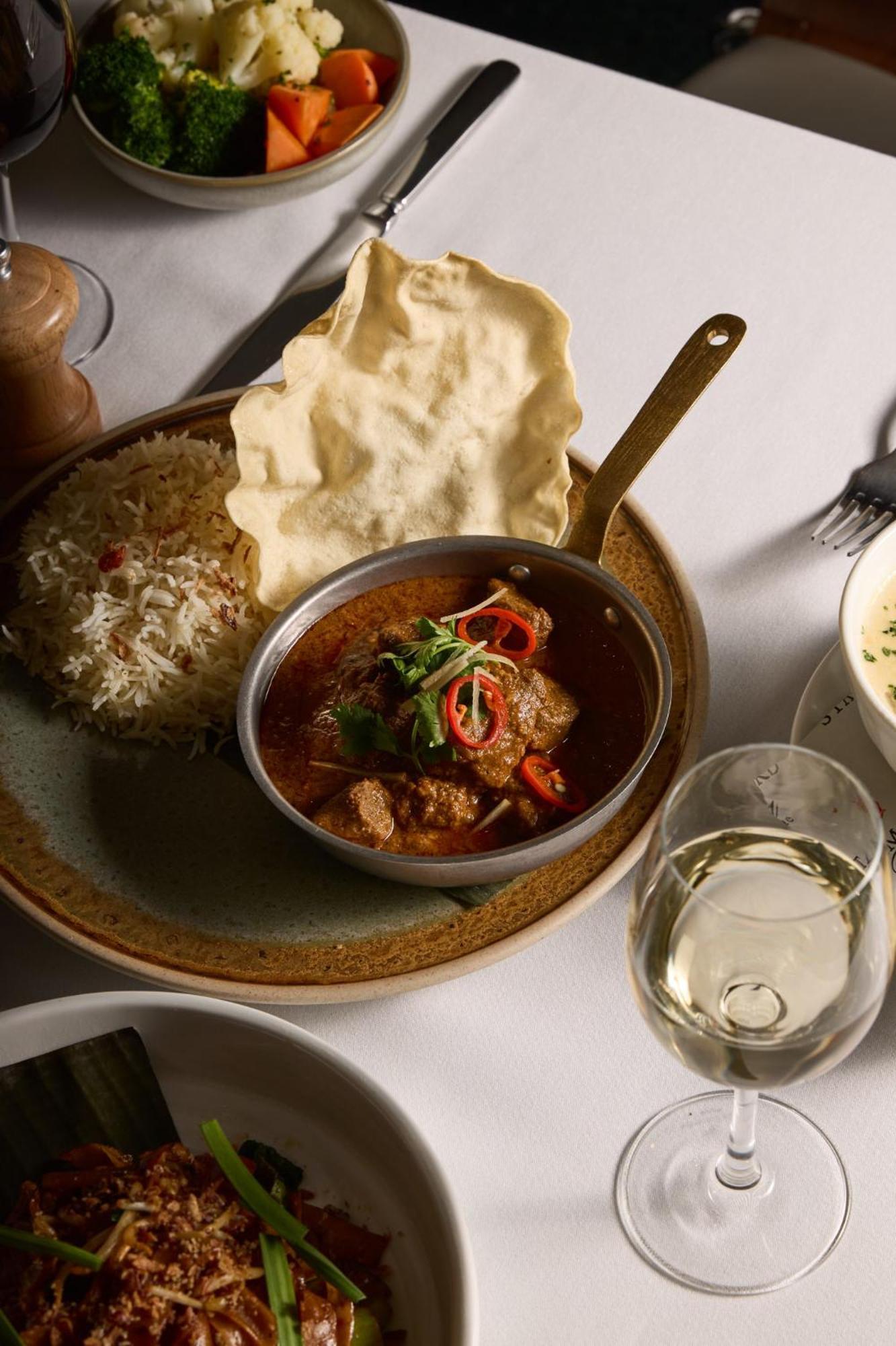 Отель Stamford Plaza Мельбурн Экстерьер фото The photo features a plated meal that includes a serving of meat curry in a small round dish. The curry is garnished with herbs and slices of chili. Accompanying the curry, there is a mound of fluffy rice, and a piece of crispy flatbread (poppadom) r