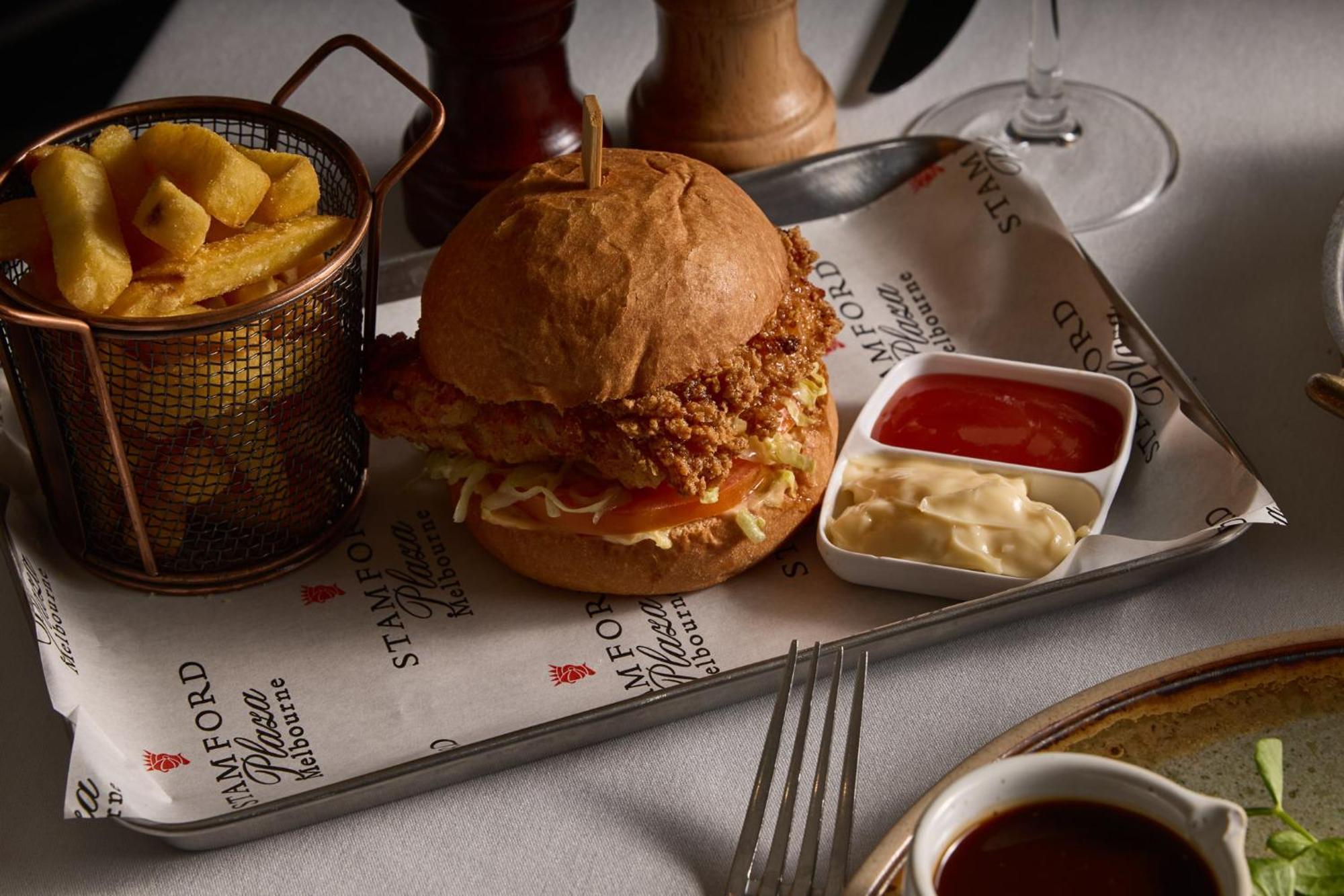 Отель Stamford Plaza Мельбурн Экстерьер фото The photo features a meal served on a tray. In the center is a sandwich made with a golden-brown chicken fillet that appears crispy, placed inside a soft bun. The sandwich is likely complemented by some type of sauce or condiments underneath the chic