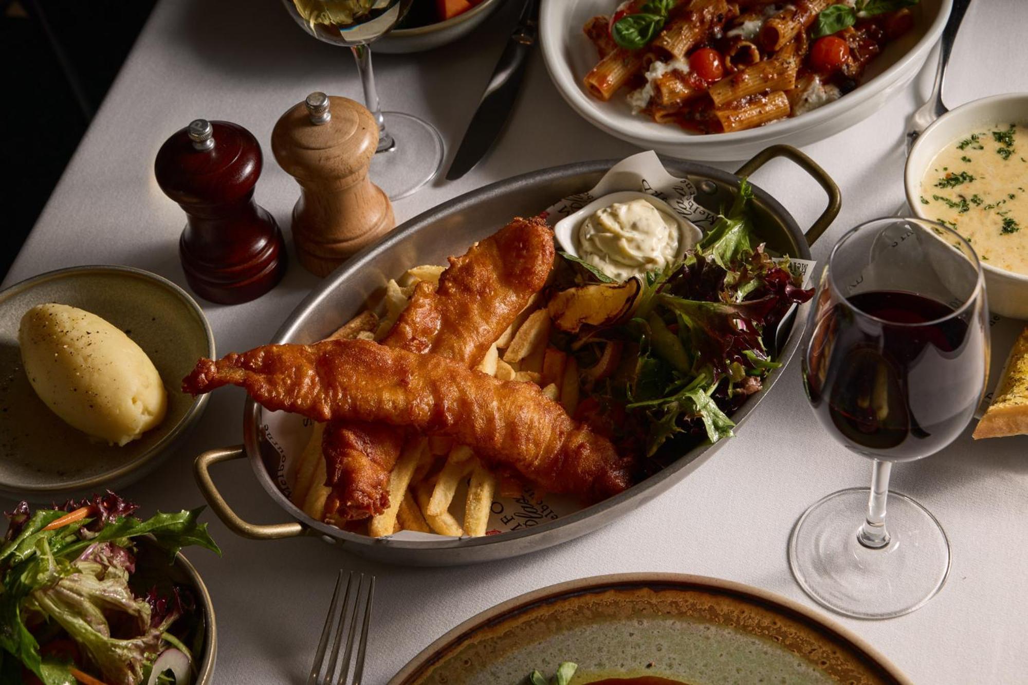 Отель Stamford Plaza Мельбурн Экстерьер фото The photo showcases a beautifully arranged meal. In the foreground, there are two pieces of golden-battered fish served with crispy fries. Accompanying the fish is a small dollop of creamy sauce and a side salad, which has a mix of greens. Surroundin