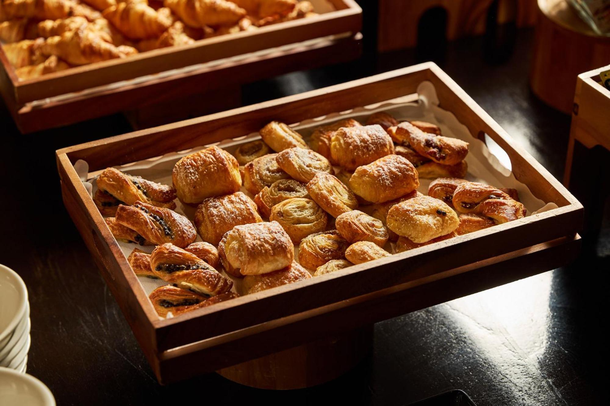 Отель Stamford Plaza Мельбурн Экстерьер фото The photo shows a wooden tray filled with an assortment of baked goods. There are various types of pastries, including small, flaky items that appear to be puff pastries, and possibly some filled with chocolate or fruit. The pastries are golden brown